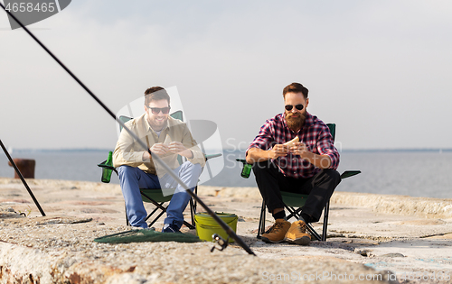 Image of happy friends fishing and eating sandwiches