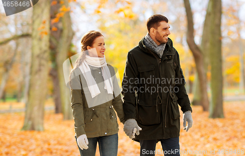 Image of couple holding hands and walking along autumn park