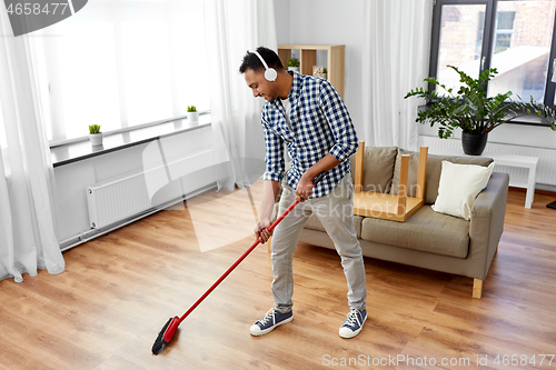Image of man in headphones with broom cleaning at home