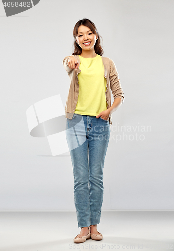 Image of asian woman pointing to you over grey background