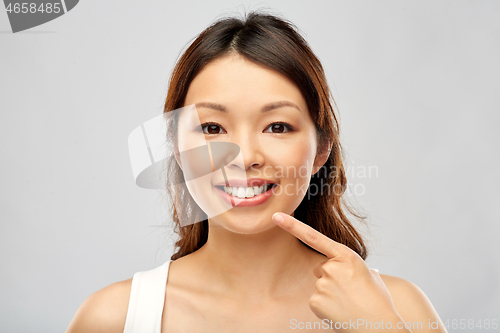 Image of happy smiling young asian woman touching her face