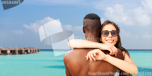 Image of happy mixed race couple hugging on summer beach