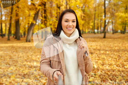 Image of woman taking picture by selfiestick at autumn park