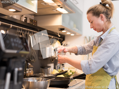 Image of Stay at home housewife woman cooking in kitchen, salting dish in a saucepan, preparing food for family dinner.