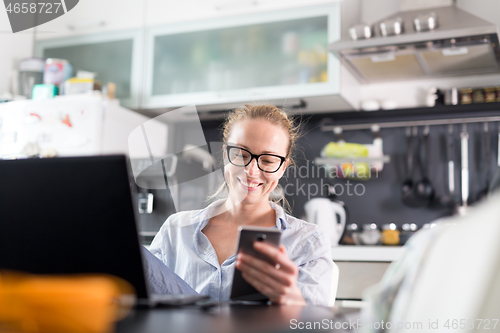 Image of Stay at home and social distancing. Woman in her casual home clothing working remotly from kitchen dining table. Video chatting using social media with friend, family, business clients or partners