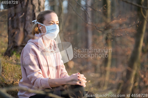 Image of Portrait of caucasian sporty woman wearing medical protection face mask while relaxing in nature and listening to music. Corona virus, or Covid-19, is spreading all over the world