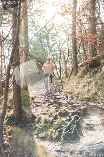 Image of Active sporty woman listening to the music while running in autumn fall forest. Female runner training outdoor. Healthy lifestyle image of young caucasian woman jogging outside