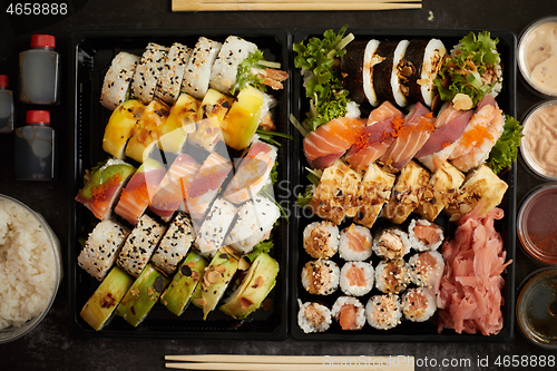 Image of Asian food delivery home, various sushi sets in plastic containers with sauces, rice and chopsticks