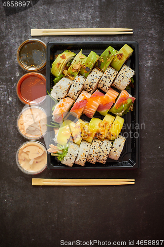 Image of Asian food delivery home, various sushi sets in plastic containers with sauces, rice and chopsticks