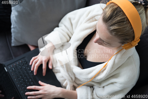 Image of Stay at home, shelter in place and social distancing. Woman in her casual home bathrobe relaxing while working remotly from her living room. Using social media apps for video chatting