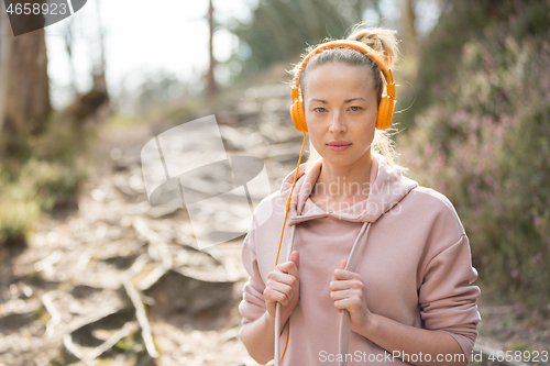 Image of Portrait of beautiful sports woman with hoodie and headphones during outdoors training session.