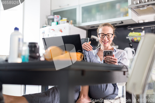 Image of Stay at home and social distancing. Woman in her casual home clothing working remotly from kitchen dining table. Video chatting using social media with friend, family, business clients or partners