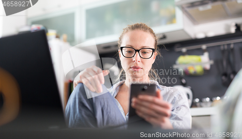 Image of Stay at home and social distancing. Woman in her casual home clothing working remotly from kitchen dining table. Video chatting using social media with friend, family, business clients or partners