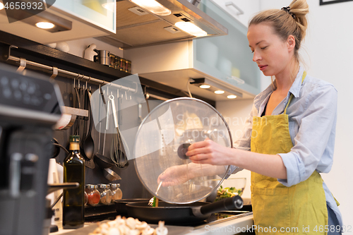 Image of Stay at home housewife woman cooking in kitchen, stir frying dish in a saucepan, preparing food for family dinner.