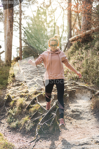 Image of Active sporty woman running in autumn fall forest jumping over the roots on the path. Healthy lifestyle image of young active caucasian woman jogging outside in nature