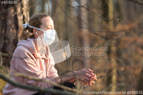 Image of Portrait of caucasian sporty woman wearing medical protection face mask while relaxing in nature and listening to music. Corona virus, or Covid-19, is spreading all over the world