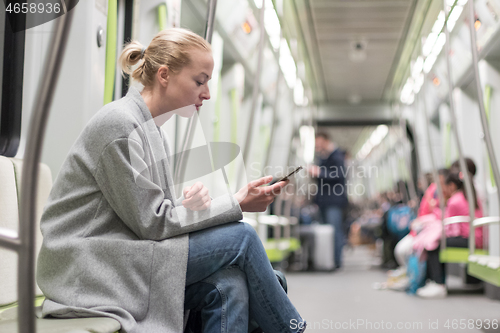 Image of Portrait of lovely girl typing message on mobile phone in almost empty public subway train. Staying at home and social distancing recomented due to corona virus pandemic outbreak