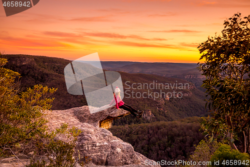 Image of Hiker sitting on edge of rock precipice with escarpment valley views