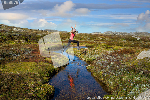Image of Woman run free jumping little meandering stream in high country