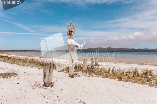 Image of Beautiful woman balance on wooden post yoga pose in swimwear and sarong