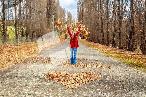 Image of Woman throwing leaves in air in front of heart of fallen leaves 