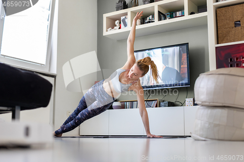 Image of Attractive sporty woman working out at home, doing pilates exercise in front of television in her living room. Social distancing. Stay healthy and stay at home during corona virus pandemic