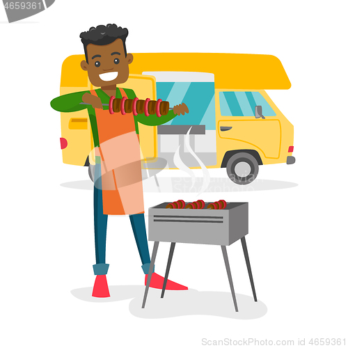 Image of Young man barbecuing meat in front of camper van.
