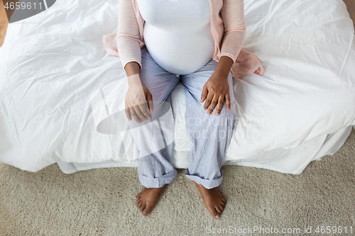 Image of pregnant african woman sitting on bed at home