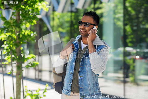 Image of man with backpack calling on smartphone in city