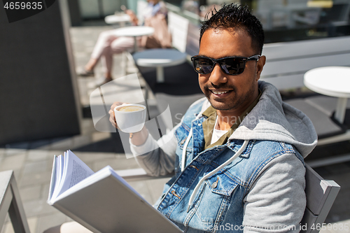 Image of man reading book and drinking coffee at city cafe