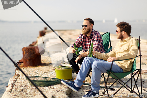 Image of happy friends fishing and drinking beer on pier