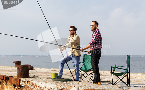 Image of male friends with fishing rods on sea pier