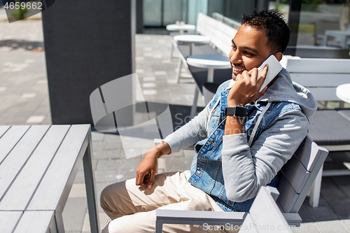 Image of indian man calling on smartphone at street cafe