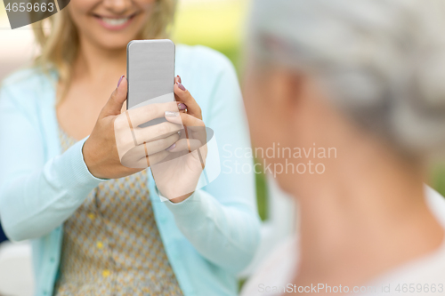 Image of daughter photographing senior mother by smartphone