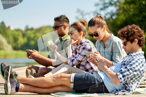 Image of friends with smartphone on lake pier in summer