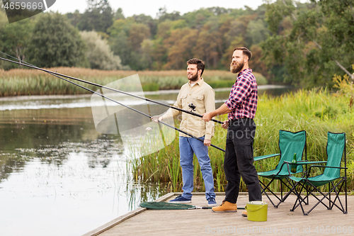 Image of male friends with fishing rods on lake pier