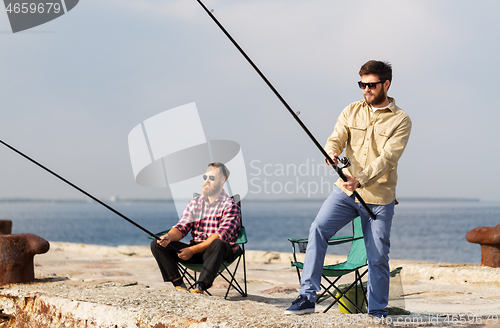 Image of male friends with fishing rods on sea pier