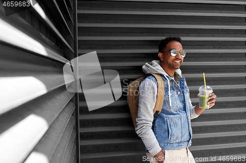 Image of man with backpack drinking smoothie on street