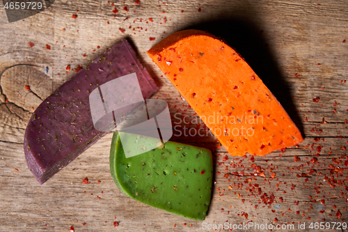 Image of Three different cheeses on rough wooden planks: lavender, paprika and pesto cheeses