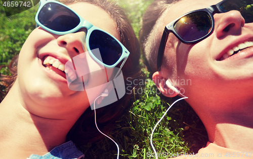 Image of happy teenage couple with earphones lying on grass