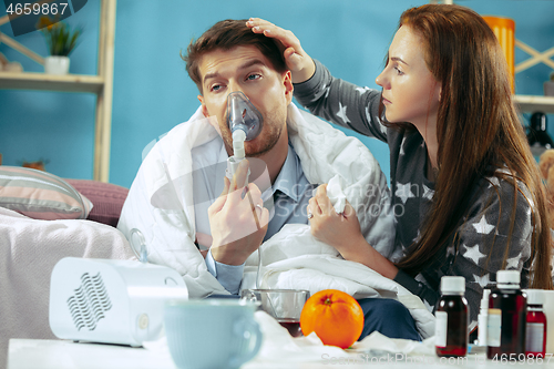 Image of Sick man with fever lying in bed having temperature girl take care for him