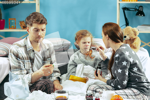 Image of The young parents with sick daughter at home. The ill family.