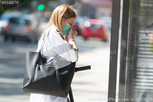 Image of Casual caucasian teenager commuter waering protective face mask against spreading of corona virus with modern foldable urban electric scooter waiting for metro city bus. Urban mobility concept