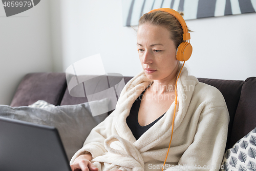 Image of Stay at home, shelter in place and social distancing. Woman in her casual home bathrobe relaxing while working remotly from her living room. Using social media apps for video chatting.