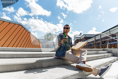 Image of indian man with pizza and drinking beer outdoors