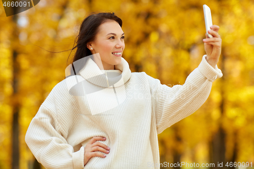 Image of woman taking selfie by smartphone at autumn park