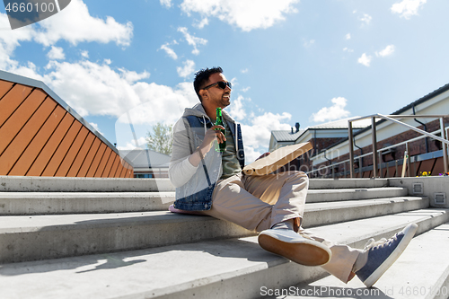 Image of indian man with pizza and drinking beer outdoors