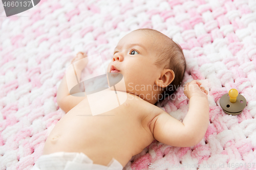 Image of baby girl in diaper lying with pacifier on blanket