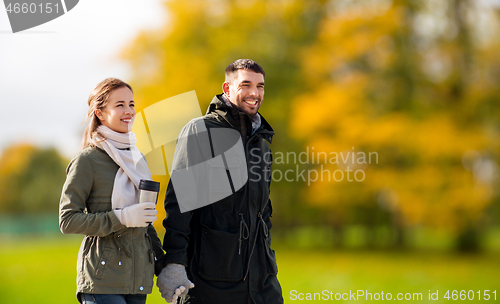 Image of couple with tumbler walking along autumn park