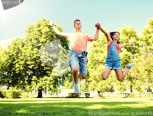 Image of happy teenage couple jumping at summer park